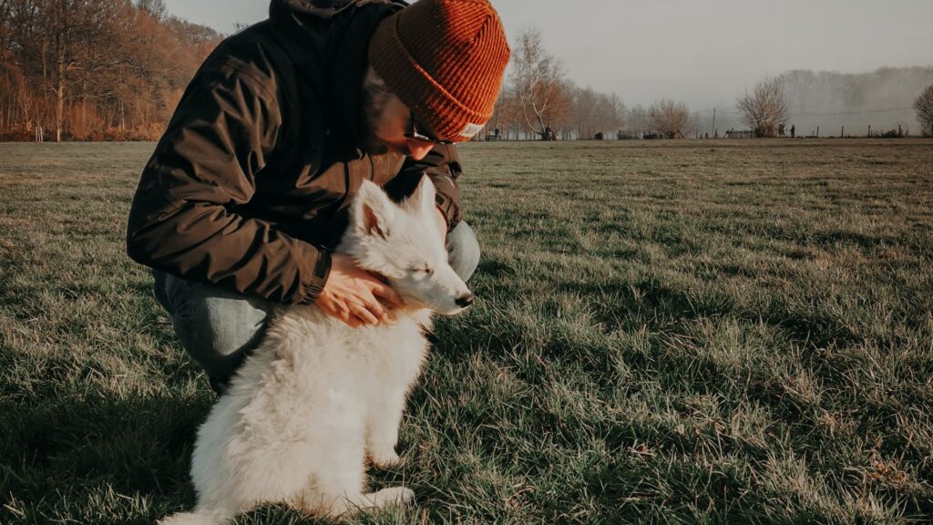 man in jacket and hat with dog in field